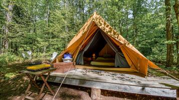 A tent set up in a forest with a table and chairs nearby.