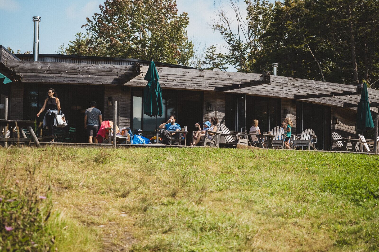 A rustic wooden building with outdoor seating and a grassy area in front.