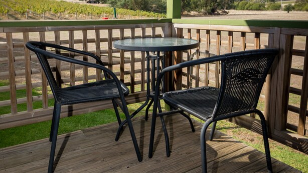 A wooden deck with two black metal chairs and a small round table, overlooking a vineyard and hills. - Blue House at Mountainside Wines (Mount Cole)