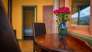 A wooden table with a blue vase containing red roses, a chair, a bed with blue bedding, and a door in the background. - Blue House at Mountainside Wines (Mount Cole)