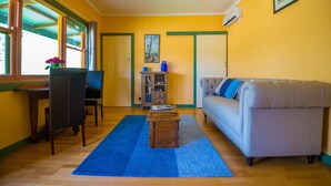A living room with a sofa, a coffee table, a bookshelf, and a dining area with chairs and a table. - Blue House at Mountainside Wines (Mount Cole)