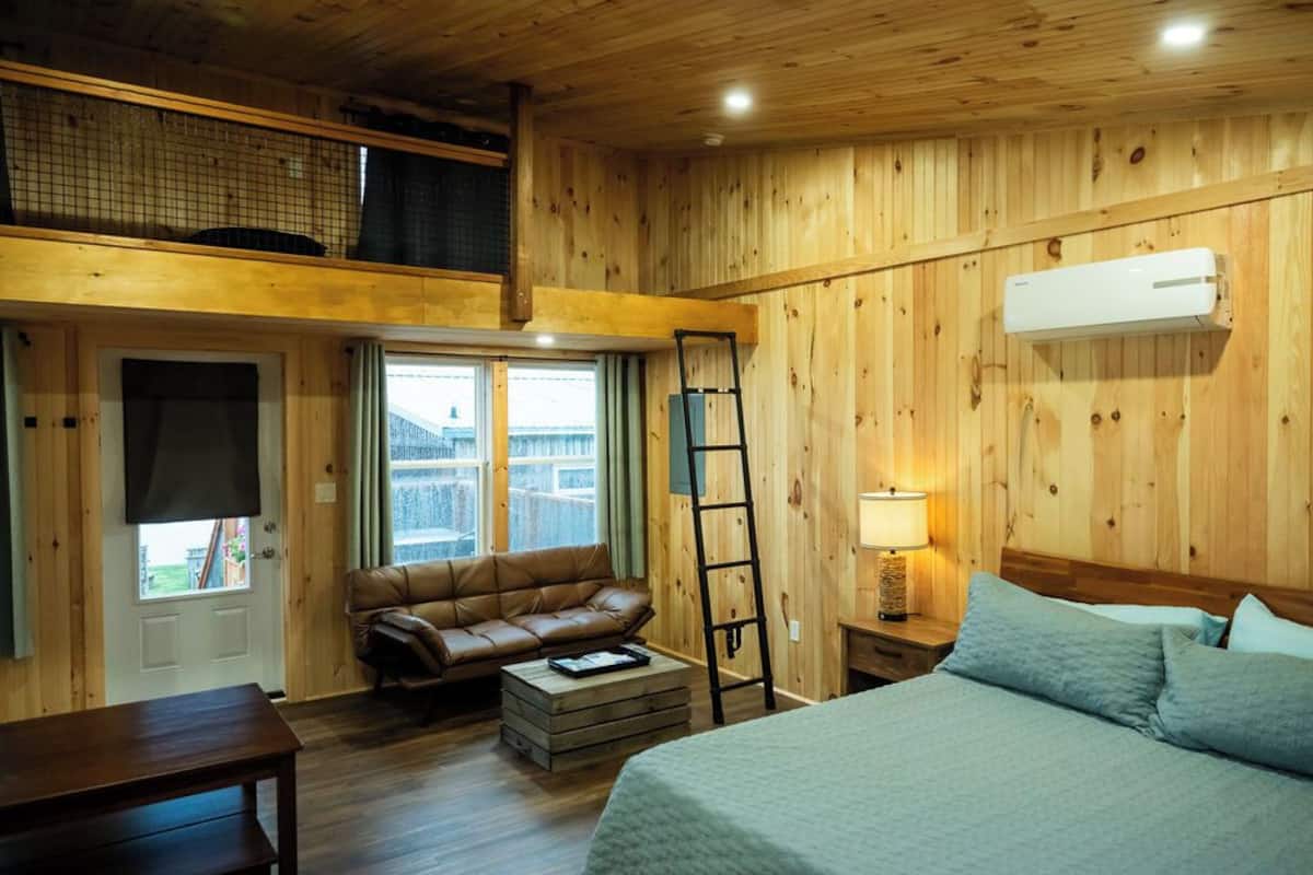 Una habitación con paneles de madera, una cama, un sofá, una escalera y una ventana.