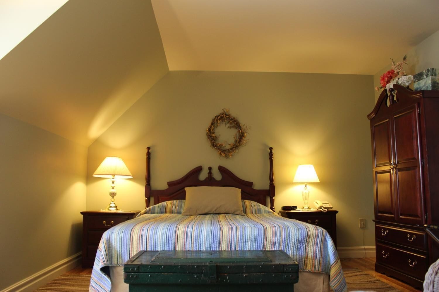 Une chambre à coucher avec un lit en bois, deux lampes de chevet, une table de chevet, une commode et un coffre vert.