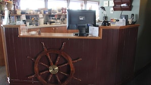 Un comptoir d’accueil orné d’un volant de navire en bois, un ordinateur et divers fournitures de bureau.