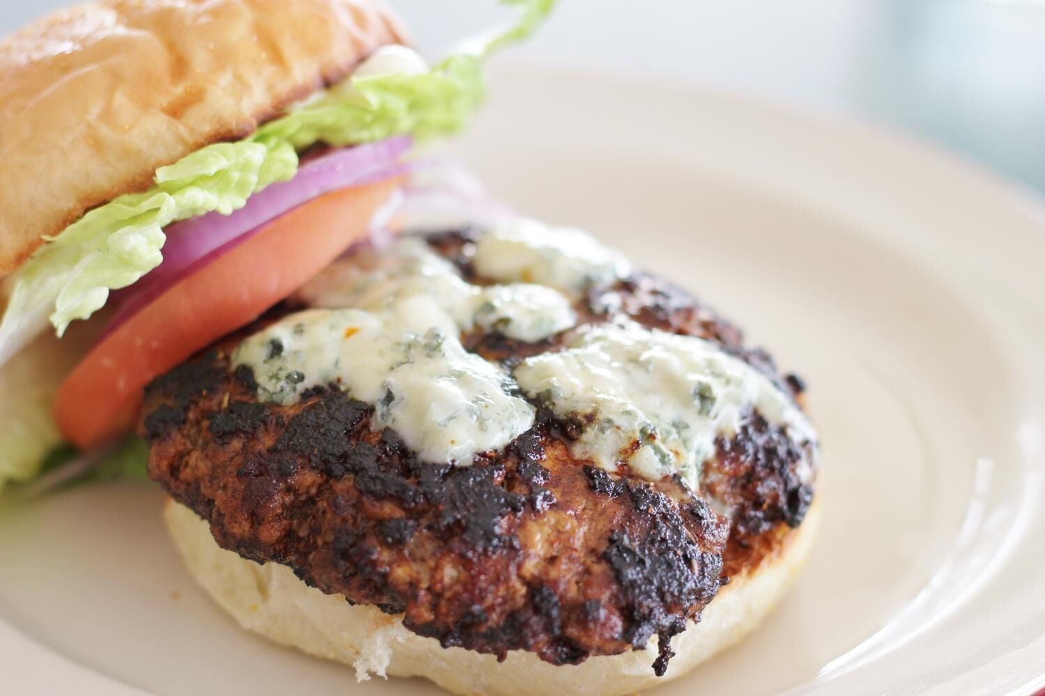 A burger with a sesame seed bun, lettuce, tomato, and red onion, topped with a creamy sauce.