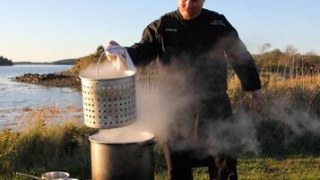 A person cooking outdoors with a portable stove, a pot, and a steaming colander.