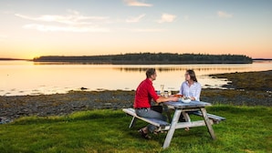 Un couple est assis à une table en bois, près d’un lac, avec une forêt en arrière-plan.