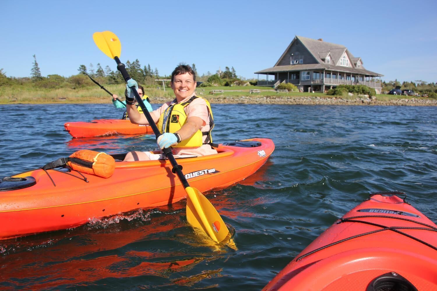 A person kayaking on a body of water with a house in the background.