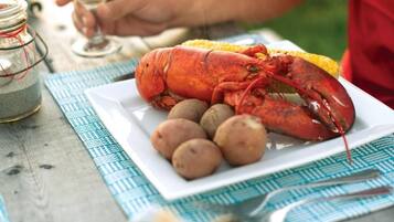 A lobster on a plate with potatoes, a glass of white wine, and a bowl of oysters on a wooden table.