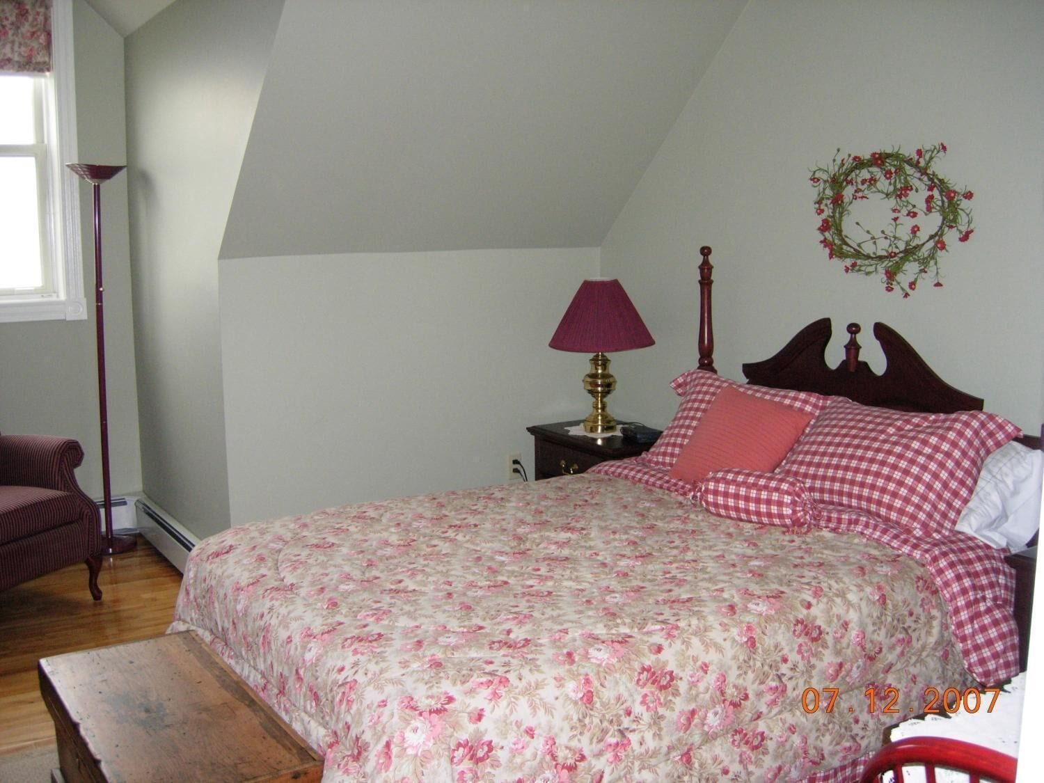 A bedroom with a bed, a nightstand, a lamp, a chair, and a window.