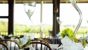 Un espace repas avec des tables dressées pour le service, agrémenté de nappes blanches, de centres de table floraux et de chaises en bois.