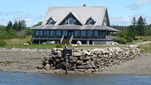 Une grande maison à plusieurs étages, dotée d’un toit en pente, située au bord d’une côte rocheuse.