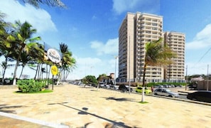 A beachfront street with high-rise buildings, palm trees, and parked cars. - Beach Village - MeuLugarCeará (Fortaleza)
