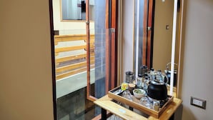 Habitación de hotel con puerta de vidrio corredera, banco de madera en el exterior y bandeja con tetera y juego de té.