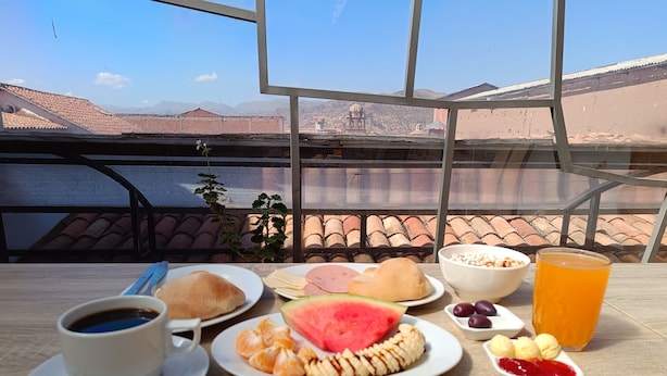 Una mesa con alimentos para el desayuno, como cruasanes, una fuente de sandía en rodajas, un tazón de cereal, un vaso de jugo de naranja y una taza de café.