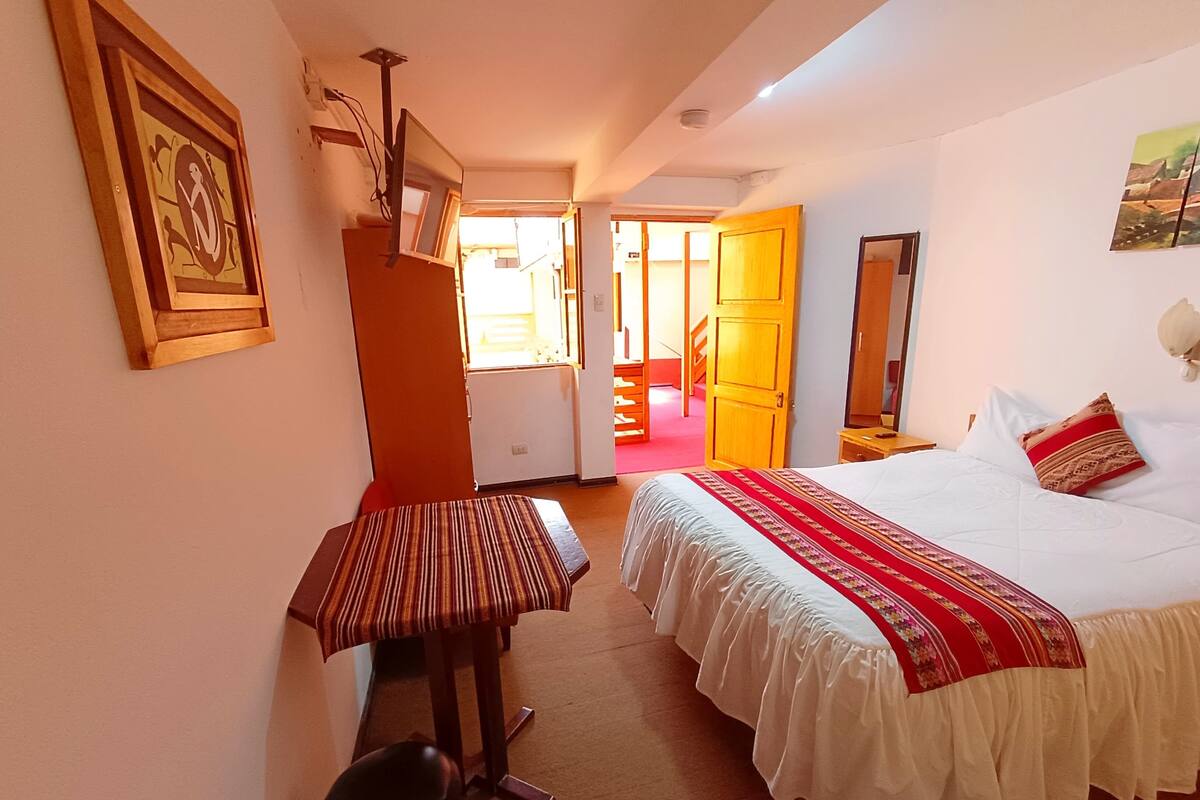 A hotel room with a bed, a desk, a chair, a mirror, and a door leading to another room.