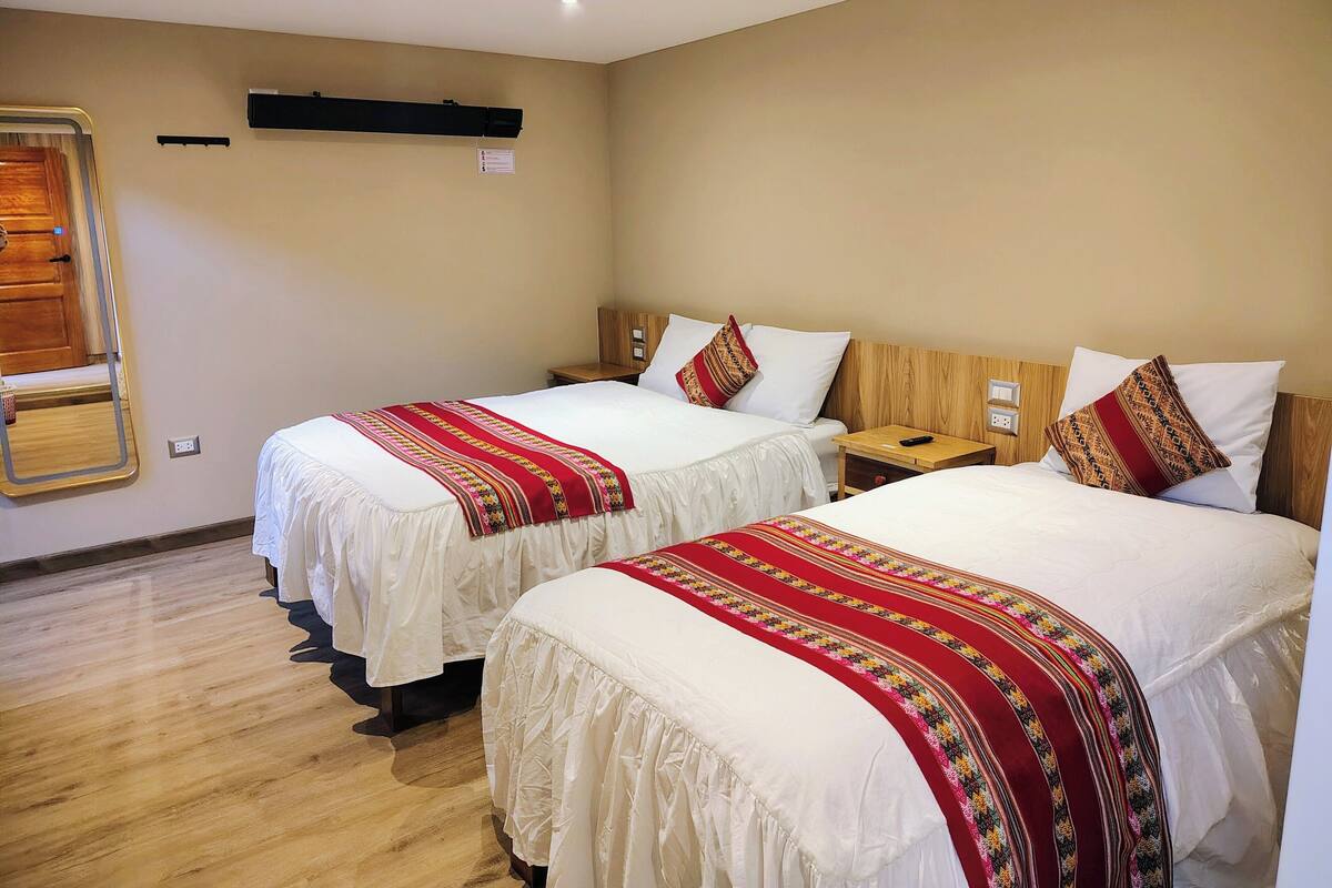 A hotel room with two beds, a wooden headboard, a bedside table, and a mirror.