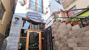 Fachada de hotel de piedra, con puerta de madera y reja de metal.