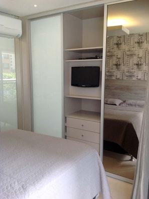 A bedroom with a bed, a television on a shelf, and a wardrobe with a mirror. - Landscape Beira Mar - MeuLugarCeará (Fortaleza)
