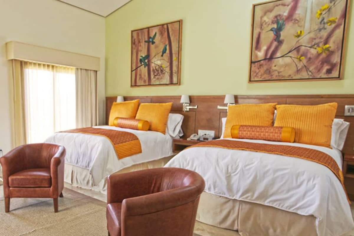 Ein Hotelzimmer mit zwei Betten, einer Sitzecke mit einem Sessel und Bildern an den Wänden.