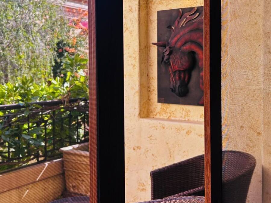 Un balcón con muebles de mimbre, un adorno en la pared y abundante vegetación.