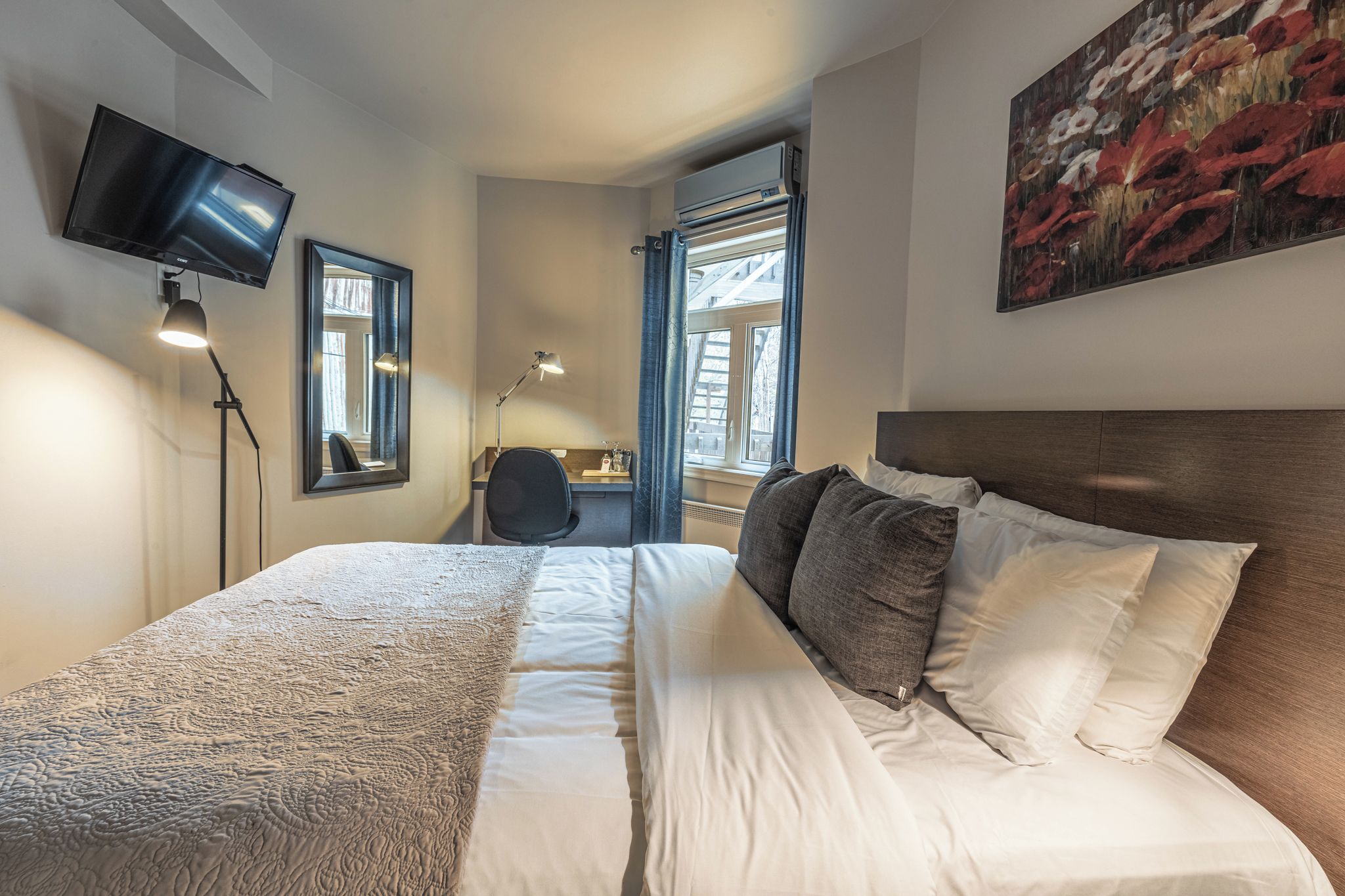Una camera d'albergo con un letto, una scrivania, una sedia, una TV a schermo piatto e un quadro appeso al muro.