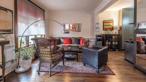 A living room with a sofa, armchairs, a coffee table, and a large window with blinds. - Petit Hôtel Café Krieghoff (Québec City)