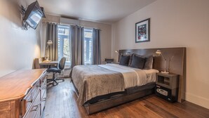 A modern bedroom with a bed, desk, and chair, a flat-screen TV mounted on the wall, and a window with curtains. - Petit Hôtel Café Krieghoff (Québec City)