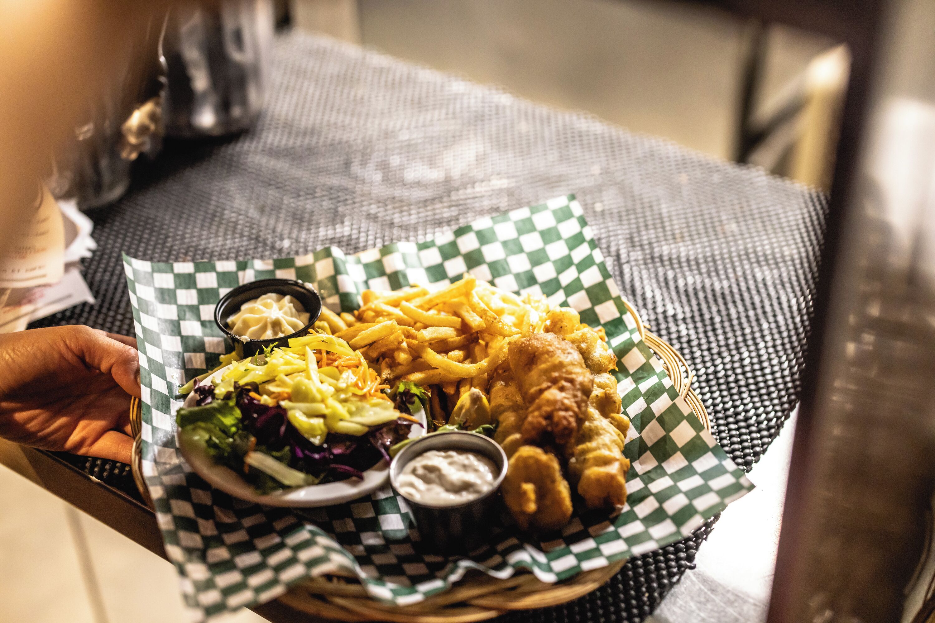 Een mand met een maaltijd bestaande uit fish and chips, frietjes, salade en twee dipsausen.