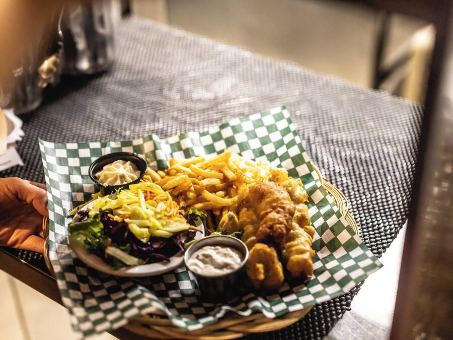 Een mand met een maaltijd bestaande uit fish and chips, frietjes, salade en twee dipsausen.