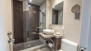 A modern bathroom with a glass-enclosed shower, a sink with a marble countertop, a toilet, and a large mirror.