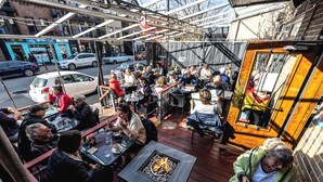 An outdoor seating area with tables and chairs, a fire pit, and a view of the street. - Petit Hôtel Café Krieghoff (Québec City)