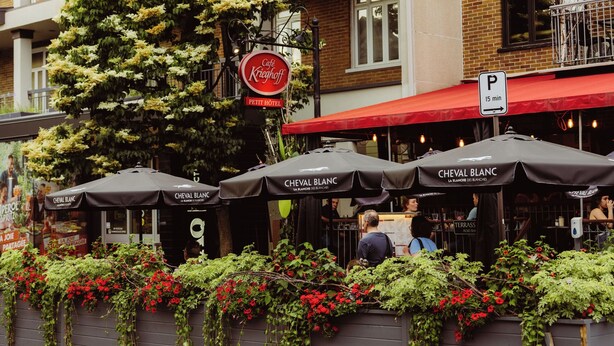 A building with a red awning and outdoor seating. There is a sign for 'Cafe Kreigoff' and a parking sign indicating 15 minutes. - Petit Hôtel Café Krieghoff (Québec City)