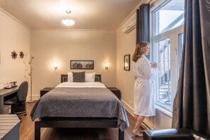 A hotel room with a bed, a desk, a chair, a window with curtains, and a painting on the wall. - Petit Hôtel Café Krieghoff (Québec City)
