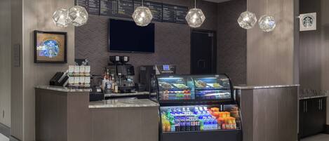 A modern Starbucks counter with a menu board above, a coffee machine, and a refrigerated display of beverages.