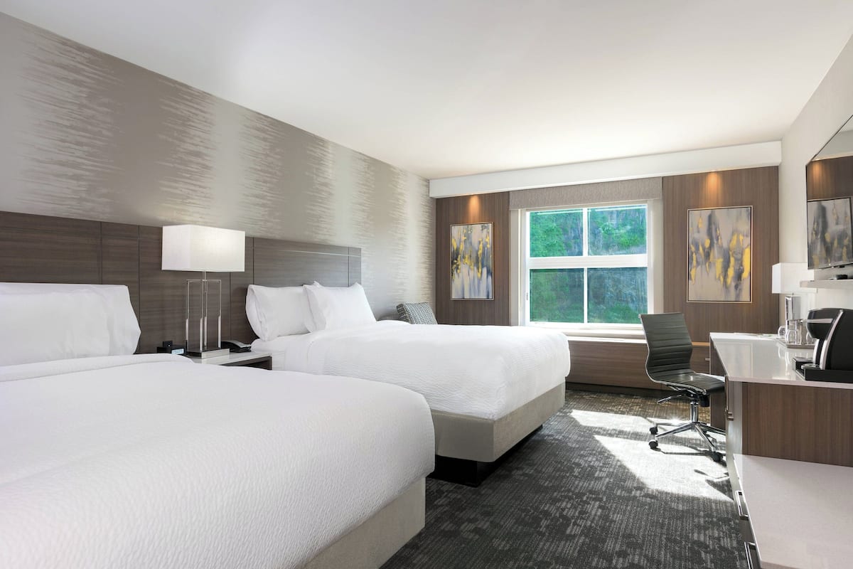A hotel room with two beds, a desk, a chair, and artwork on the walls.