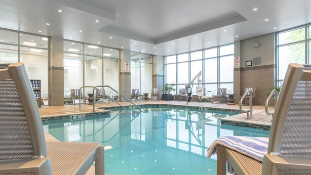 Une piscine intérieure à l’eau claire, entourée de chaises longues et dotée d’un mur en verre.