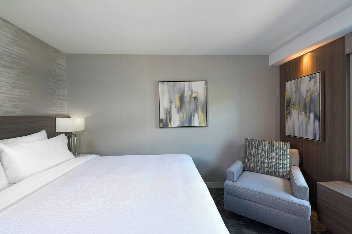 A hotel room with a large bed, a chair, and two abstract paintings on the wall.