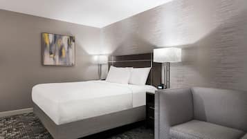 A hotel room with a bed, two bedside lamps, a chair, and a painting on the wall.