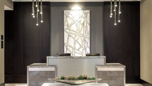 Un espace d’accueil au design moderne, comprenant un comptoir de réception en marbre, une grande œuvre d’art abstraite au mur et un élément décoratif au centre de la pièce.