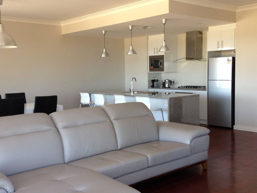 A modern living room with a large sectional sofa, a dining area with a table and chairs, and a kitchen area with a refrigerator and microwave.