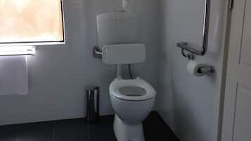 Un baño con inodoro blanco, barra de apoyo y ventana.