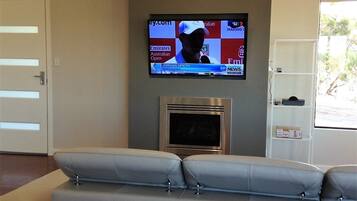 Ein modernes Wohnzimmer mit einem grauen Sofa, einem flachbildfernseher an der Wand und einem Kamin darunter.