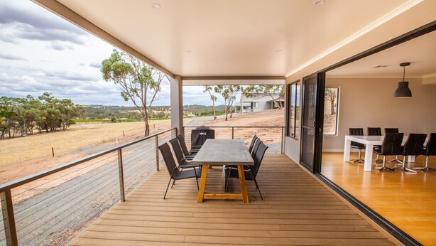 Un balcon spacieux doté d’un plancher en bois, d’une table à manger avec des chaises et offrant une vue sur la campagne.