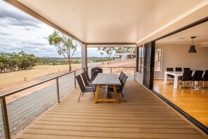 A spacious balcony with a wooden floor, a dining table with chairs, and a view of the countryside. - Neagles Retreat Villas (Emu Flat)