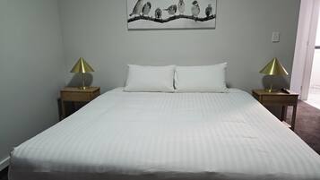 A neatly made bed with white linens, two bedside tables with lamps, and a wall-mounted artwork of birds.