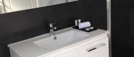 Une salle de bain moderne avec un meuble-lavabo blanc, un grand miroir et une cabine de douche en verre.