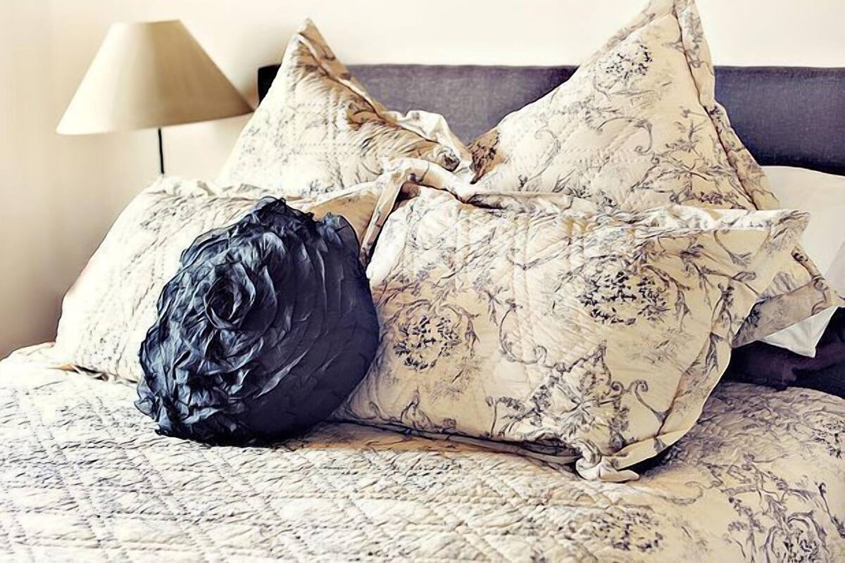 A bed with floral patterned bedding, a dark blue pillow, and a lamp in the background.