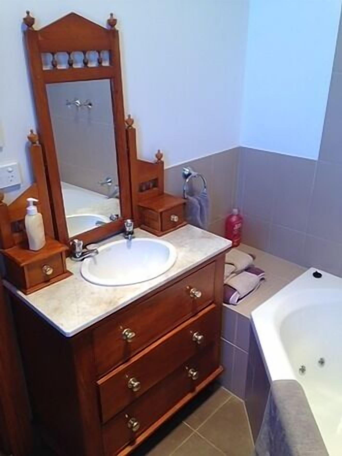 A bathroom with a wooden vanity, a sink, a mirror, and a bathtub.