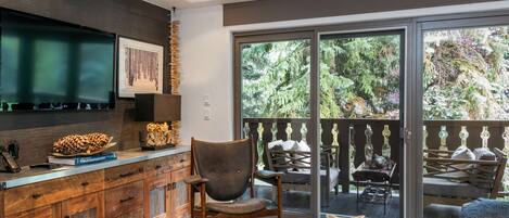 Un salon moderne doté d’un grand téléviseur, de meubles en bois, d’un coin salon confortable et d’un balcon aménagé avec du mobilier d’extérieur.